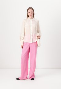 Long-sleeve, light cream blouse with lace detailing and buttons, paired with high-waisted, wide-leg pink trousers and black shoes.