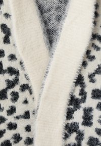 Närbild av mjuk stickad tröja med krämfärgad sjalkrage och svart-vit leopardmönster.