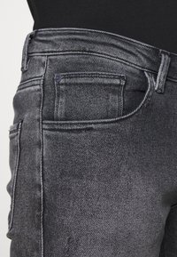 Jeans de mezclilla negra con un diseño clásico de cinco bolsillos, silueta ajustada y textura sutil. Costuras expuestas y herrajes estándar.