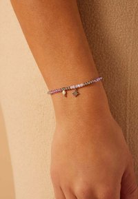 Kralenarmband met roze en paarse kralen, zilveren balletjes als accenten en een kleine zilveren ster charm op een huidtint pols.