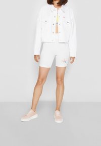 Valkoinen denimi lyhyt takki, valkoiset pyöräilyshortsit, joissa on "Tämä on rakkautta" grafiikka, sekä vaaleanpunaiset lenkkarit, joissa on valkoiset pohjat. Sujuva rakenne ja istuva muotoilu.