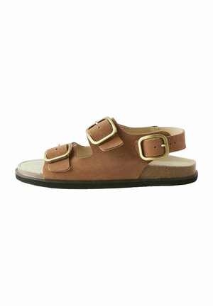 Sandal in suede marrone con due cinghie regolabili e una cinghia posteriore, dotato di una suola piatta e fibbie in tonalità oro.