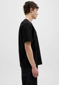 Sort bomulds T-shirt med afslappet pasform, kortærmede og rund hals. Teksturen er glat, og stoffet fremstår blødt og let.