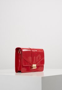 Czerwana torebka z lakierowanej skóry o strukturalnym kształcie, z zapięciem w kolorze złotym i kanciastą klapą. Posiada odpinany pasek na ramię.