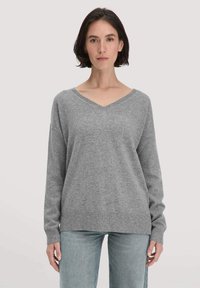 Grauer V-Ausschnitt-Pullover mit langen Ärmeln, aus weichem Stoff gefertigt, mit gerippten Bündchen und Saum, kombiniert mit hellblauen Jeans.