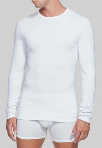 Camicia bianca a maniche lunghe e boxer bianchi realizzati in tessuto morbido e elastico. La camicia ha un collo rotondo e un design aderente.