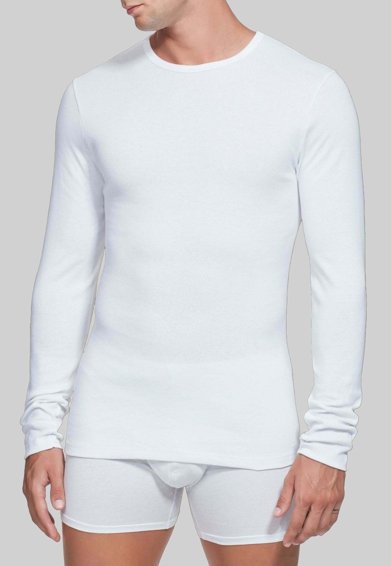 Camicia bianca a maniche lunghe e boxer bianchi realizzati in tessuto morbido e elastico. La camicia ha un collo rotondo e un design aderente.