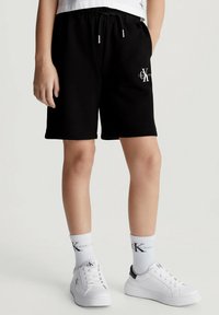 Shorts neri di cotone con fascia elastica in vita e dettagli con logo. Abbinati a sneakers bianche e calzini con stampa logo.