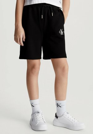 Shorts neri di cotone con fascia elastica in vita e dettagli con logo. Abbinati a sneakers bianche e calzini con stampa logo.