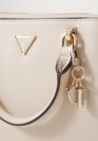 Borsa in sintetico beige con finitura testurizzata, caratterizzata da un logo triangolare dorato, dettagli neri e hardware dorato con charm.