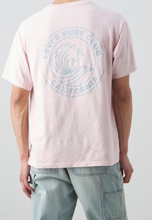 Person wearing light pink Levi’s Surf Club California T-shirt and light blue denim cargo pants, shown from the back.
