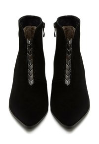 Botas de tobillo de ante negro con punta afilada, que presentan una cremallera central adornada con acentos metálicos en forma de chevron. Forro interior suave.