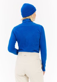 Königsblaues, geripptes Rollkragenshirt und passende Strickmütze. Figurnahes Design mit langen Ärmeln. Helle, hochtaillierte Hosen mit elastischem Bund.