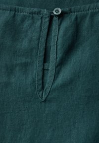 Zielona lniana tkanina z plisą z guzikiem w pasującym kolorze, ukazująca miękką fakturę i subtelny wzór tkaniny.