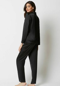 Svart satin pyjamas-set med långärmad topp och lösa byxor, båda med en slät textur och minimalistisk design.