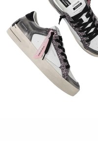 Sneaker bianchi e neri con un accento glitterato viola. Presentano una tomaia in pelle liscia con una suola in gomma e lacci neri.