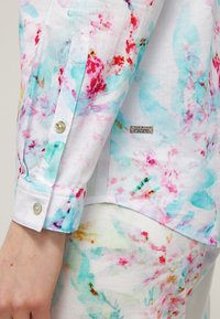 Kortebloem shirt in witte katoen met een kleurrijk bloemenpatroon in aqua, roze en rood; beschikt over een knoopmanchet en een logo label.