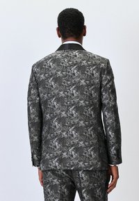 Black and white patterned suit with a floral design, featuring a single vent, black lapels, and button accents, viewed from the back.