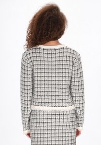 Fekete-fehér kutyafog mintás gyapjú keverék kardigán. Kerek nyakkivágással, hosszú ujjakra és bojtos díszítéssel a hemnél és a mandzsettán.