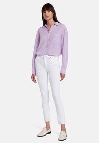 Chemise boutonnée lavande à manches longues avec une poche sur la poitrine, associée à un jean skinny blanc et des mocassins crème. Tissu léger et lisse.