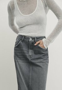 Haut ajusté à manches longues en tissu transparent de couleur blanche avec un col rond. Jupe en denim gris foncé taille haute avec une fermeture à boutons et des poches avant.