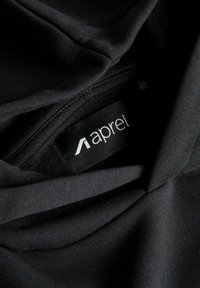 Črni zloženi tkanini z vidno črno etiketo oblačila, na kateri je bel logotip "A" in del besede "apparel".