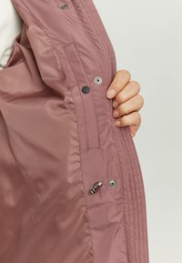 Light pink padded jacket interior with smooth texture. Features snap buttons, metal hardware, and a practical pocket design.