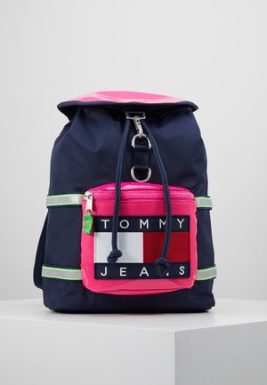 Sac à dos bleu marine avec poche avant rose, bretelles vertes réfléchissantes, fermeture par cordon, fermoir en métal et marque "Tommy Jeans" sur la poche.