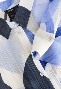 Skjorte med knapper og abstrakte farveblokke i blå, hvid og sort, med op-foldet ærme og krave med en synlig mærkeetiket indeni.