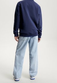 Felpa blu navy con polsini e orlo a coste indossata con jeans chiari a gamba larga e sneakers bianche con dettagli blu.