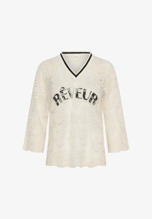 Crèmewit kanten top met lange mouwen, voorzien van een zwart-wit gestreepte V-hals en "RÊVEUR" in zwart verweerd lettertype op de borst.