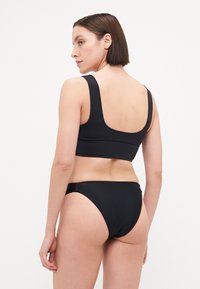 Melnā bikini komplekts, kas sastāv no topa ar apaļo kakla izgriezumu un platām siksnām, kā arī zemas apkakles apakšdaļas. Gluda tekstūra, minimālistisks dizains un bez redzamām apdrukām.