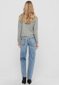 Maglione grigio chiaro con polsini a coste, abbinato a jeans blu a vita alta con tasche posteriori e gamba dritta. Stivali neri con tacco.