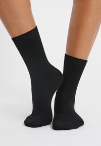 Calcetas de algodón negras con un puño acanalado, de longitud media a la pantorrilla, textura suave y diseño de punta sin costuras.