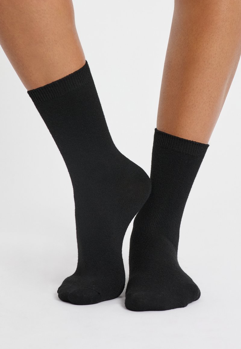 Calcetas de algodón negras con un puño acanalado, de longitud media a la pantorrilla, textura suave y diseño de punta sin costuras.