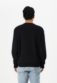 Black, long-sleeve sweatshirt with a round neckline. Made of soft material, featuring a relaxed fit and ribbed cuffs, worn with light blue jeans.