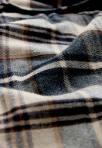 Wollstoff mit einem karierten Muster in Blau, Beige und Braun. Die Textur ist weich und leicht flauschig, mit sichtbaren, ineinander verwobenen Fasern.