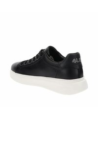 Zapatilla de cuero negro con punta redondeada, suela de goma blanca y cinco ojales. Presenta un logo en el talón y una textura suave en toda la superficie.