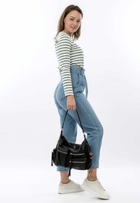 Sac en cuir noir avec plusieurs poches zippées et des détails de franges, associé à un jean en denim bleu taille haute et des baskets blanches.