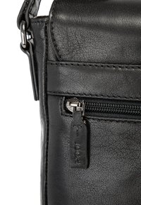 Černá kožená crossbody taška s texturovaným povrchem, přední kapsou na zip a kovovým táhlem zipu s logem.