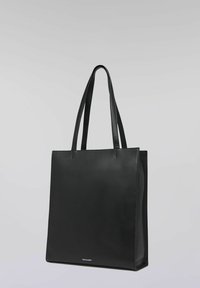 Svart läderväska med två långa handtag, minimalistisk design, slät yta och platt botten. Har en logotyp längst ner fram.