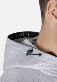 Sivi dukserica s zategnutom špagu, koja ima glatku teksturu i metalne akcenta. Unutrašnjost prikazuje crni logo trak.