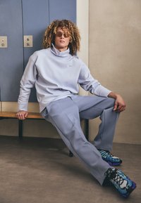 Lyseblå oversized sweatshirt med høy krage, matchende løs bukse og mønstrede svarte, blå og grønne treningssko.