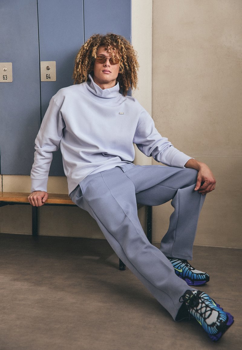 Felpa oversize azzurro chiaro con colletto alto, pantaloni larghi abbinati e scarpe da ginnastica a motivi neri, blu e verdi.