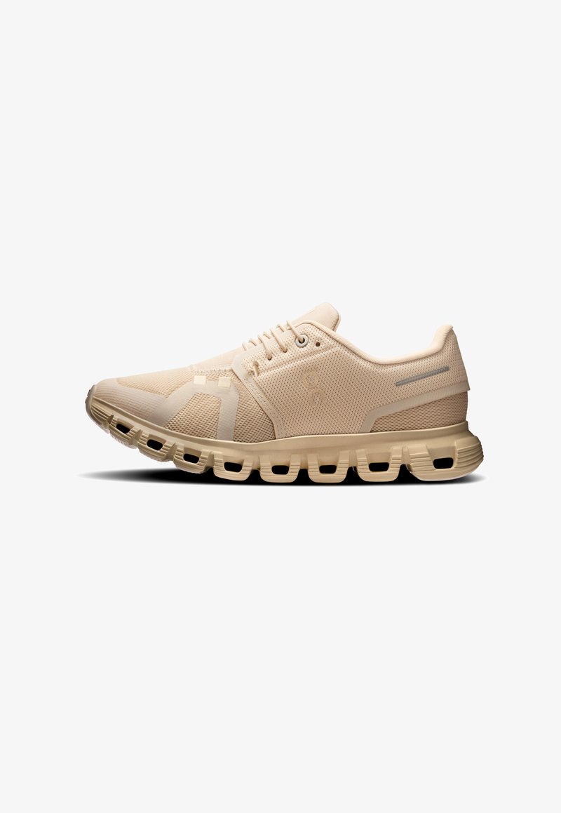 Beiger Sportschuh zum Laufen mit atmungsaktivem Mesh-Obermaterial und segmentierter, gepolsterter Sohle, im Profil vor weißem Hintergrund abgebildet.