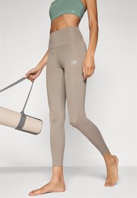 Béžové legíny s vysokým pasem vyrobené z elastického materiálu, s nenápadným logem a hladkou texturou, v kombinaci se světle zelenou sportovní podprsenkou.