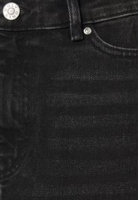 Černá denimu tkanina s jemnou strukturou, s detaily v podobě stříbrného knoflíku a nýtu. Detailní pohled na oblast pasu a kapsy.