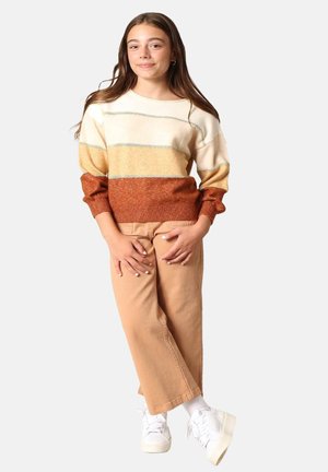 Gebreid sweater met horizontale strepen in crème, geel en oranje-bruin, gecombineerd met lichtbeige broek en witte sneakers.