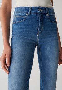 Jeans in denim blu slim con vita media, leggere sbiaditure e dettagli di cucitura sottili. Presenta tasche anteriori e chiusura con bottone.