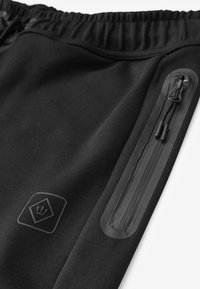 Zwarte sportbroek met een elastische tailleband, voorzien van een zijzak met een waterdichte rits en een subtiele logopatch. Zachte stoffen textuur.